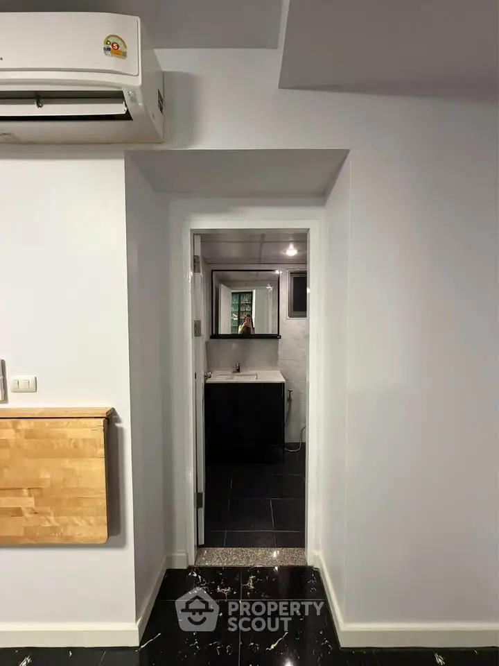 Modern interior with sleek black flooring and compact bathroom view, featuring air conditioning and minimalist design.
