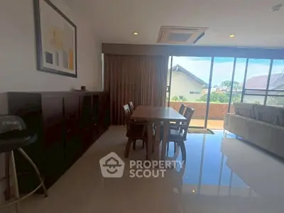 Spacious living room with dining area and large windows offering natural light and outdoor view.