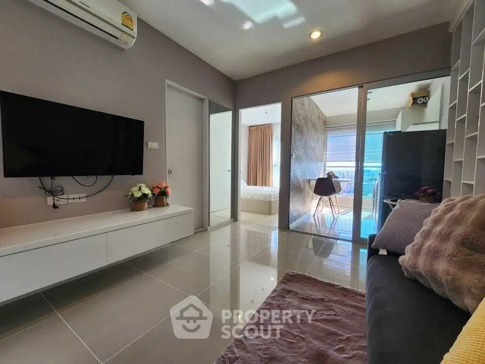 Modern living room with sleek design, featuring a wall-mounted TV, cozy seating, and access to a bright bedroom.