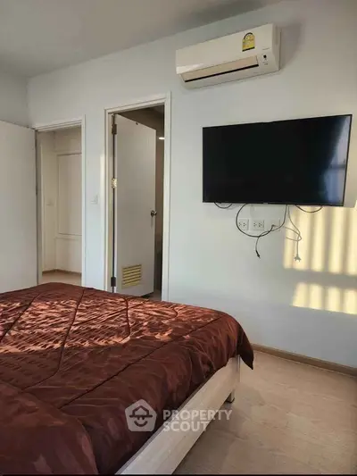 Modern bedroom with wall-mounted TV and air conditioning unit, featuring a cozy bed with brown bedding.
