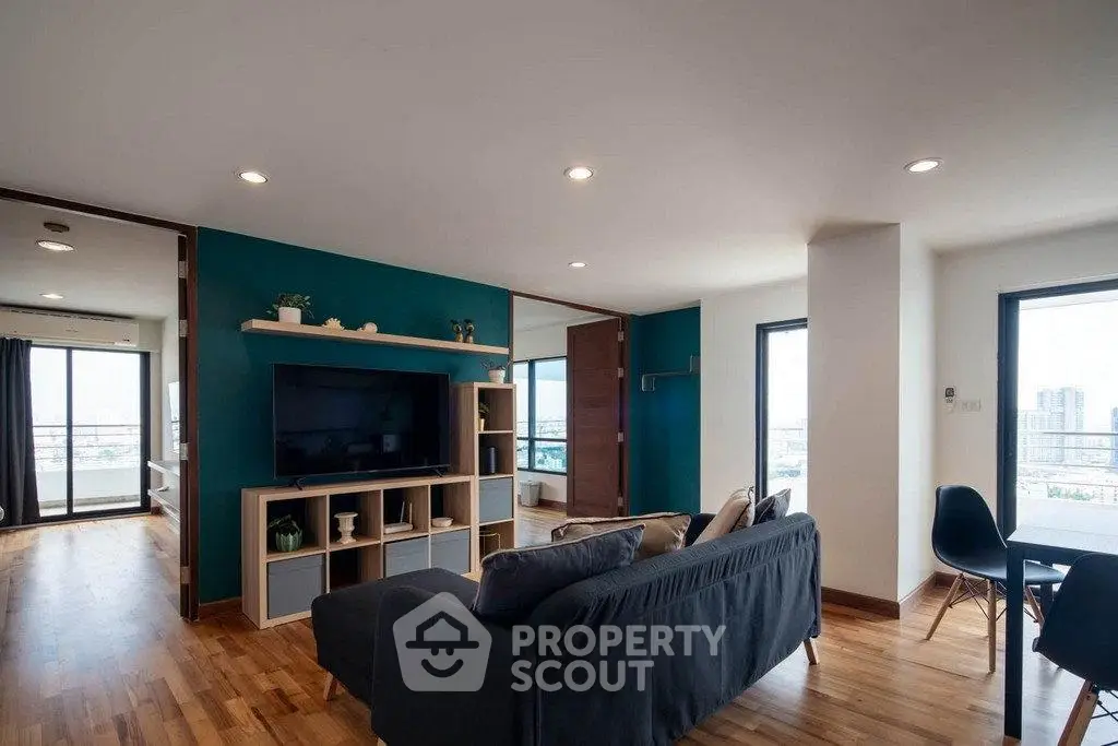Spacious modern living room with wooden flooring and large windows offering city views.