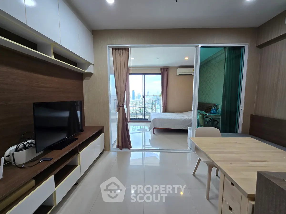 Modern apartment interior with open layout, featuring a living area, dining table, and bedroom with city view.
