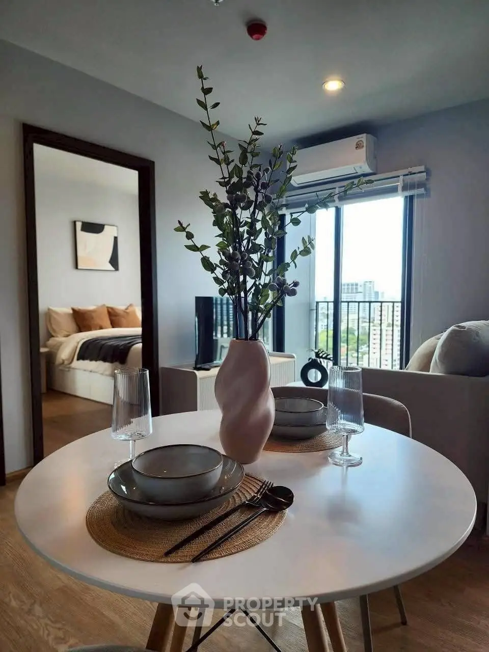 Modern living room with stylish decor and city view, featuring a cozy dining area and elegant bedroom.