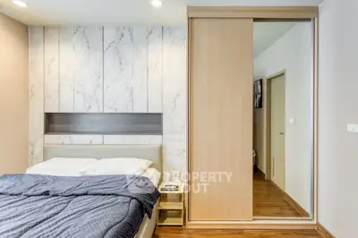 Modern bedroom with sleek design and wooden flooring, featuring a sliding door wardrobe and elegant wall paneling.