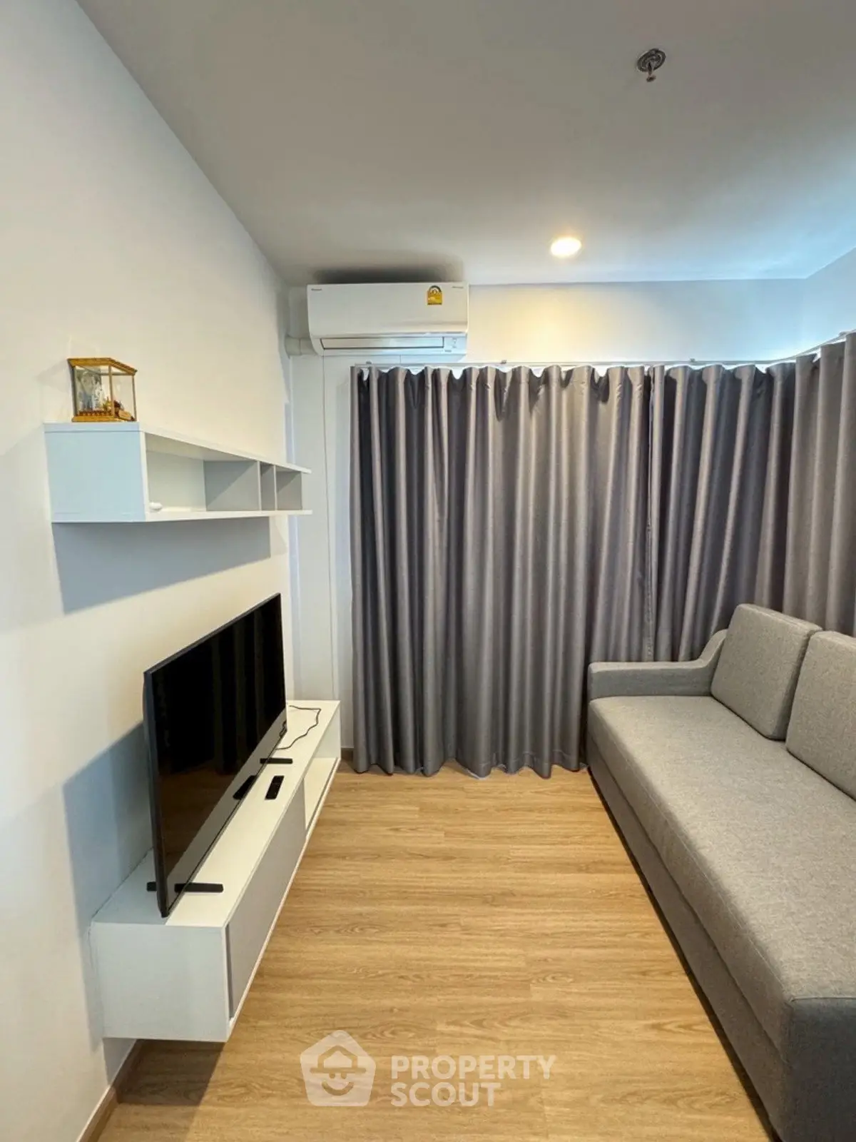 Modern living room with sleek gray sofa and wall-mounted TV unit, featuring elegant curtains and wooden flooring.