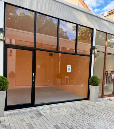 Modern commercial storefront with large glass windows and potted plants, ideal for retail or office space.