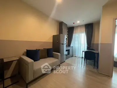Modern living room with cozy sofa and kitchenette, featuring natural light from large windows.
