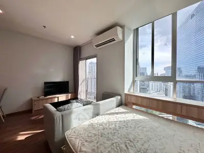 Modern living room with large windows offering stunning city views, featuring a cozy sofa and sleek TV setup.