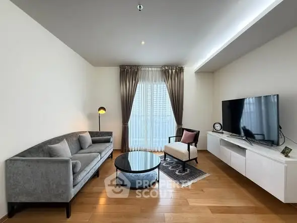 Modern living room with stylish furniture and large TV, featuring elegant curtains and wooden flooring.