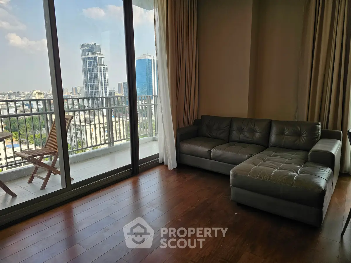 Spacious living room with large windows and balcony offering stunning city views.