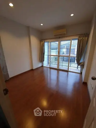 Spacious empty room with wooden flooring and large windows in modern apartment.