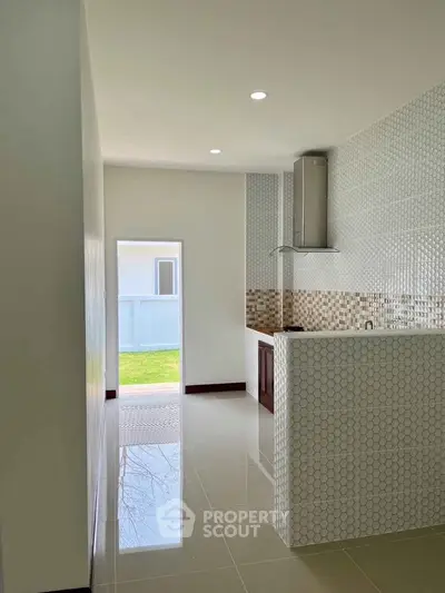 Modern kitchen with sleek tile backsplash and open layout, featuring ample natural light and glossy flooring.