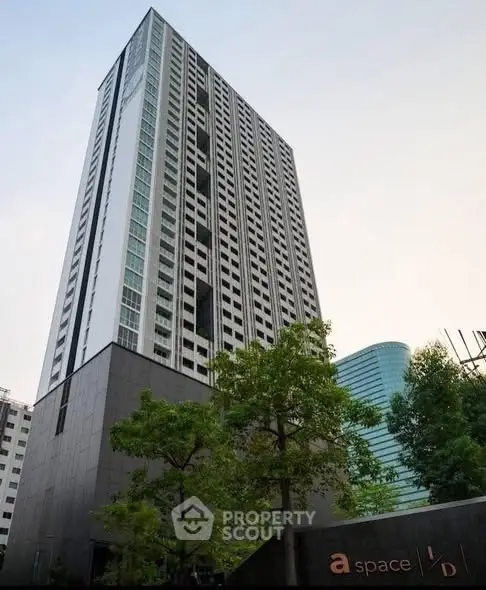Modern high-rise building with sleek design and lush greenery in urban setting.