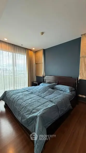 Spacious bedroom with elegant dark wood flooring and large window offering natural light.