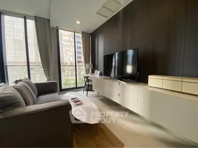 Modern living room with large windows, sleek furniture, and a flat-screen TV in a high-rise apartment.