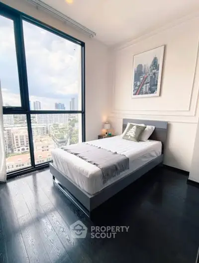 Modern bedroom with large window offering stunning city views, featuring sleek dark flooring and stylish decor.