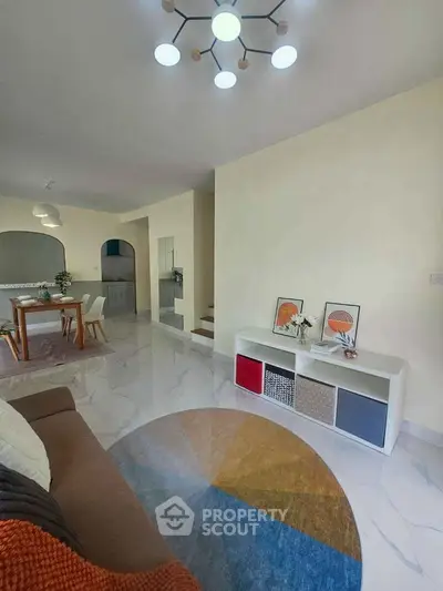Modern living room with stylish decor and open dining area, featuring a unique circular rug and contemporary lighting.