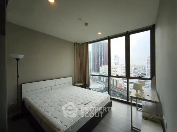 Modern bedroom with large windows offering city view, featuring a stylish bed and sleek decor.