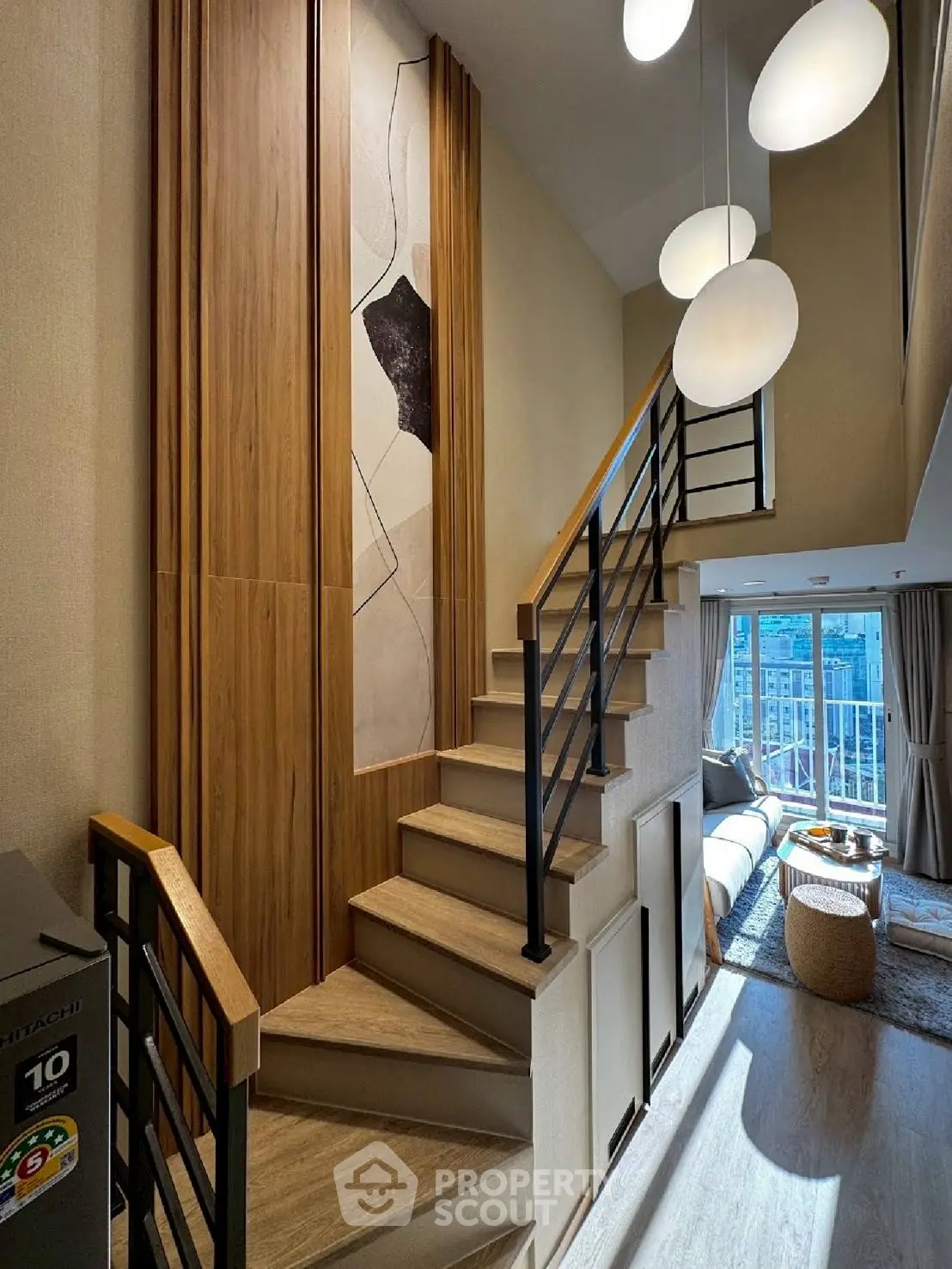 Modern duplex living room with stylish staircase and large windows offering natural light.