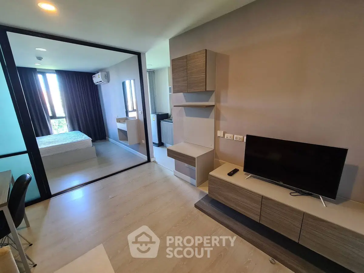Modern apartment interior with open living room and bedroom, featuring sleek furniture and natural light.
