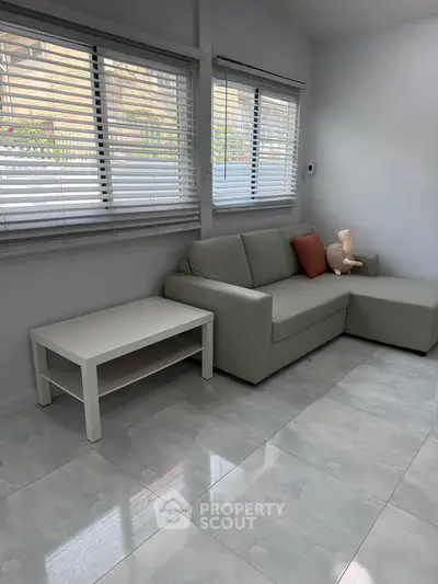 Modern living room with sleek sofa and coffee table, featuring large windows and stylish flooring.