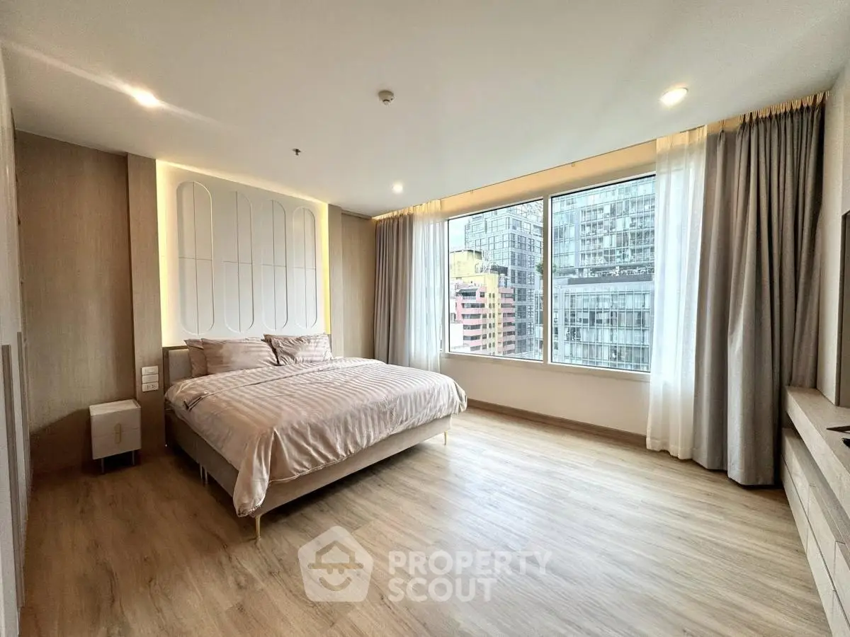 Spacious modern bedroom with large window and city view, featuring elegant decor and natural light.