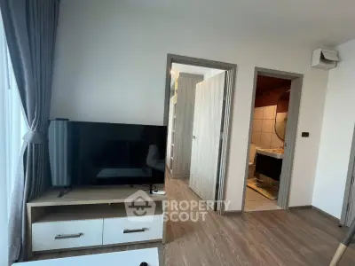 Modern living room with TV and wooden flooring, adjacent to bathroom and bedroom.