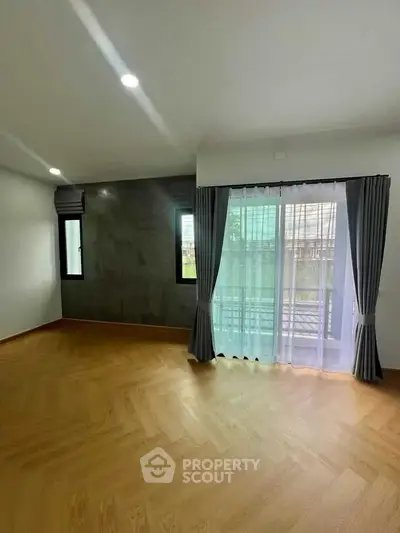 Spacious empty room with wooden flooring and large windows for natural light.