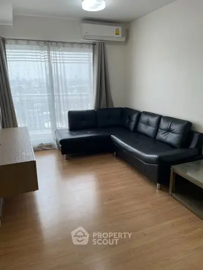 Modern living room with black leather sofa and large window view.