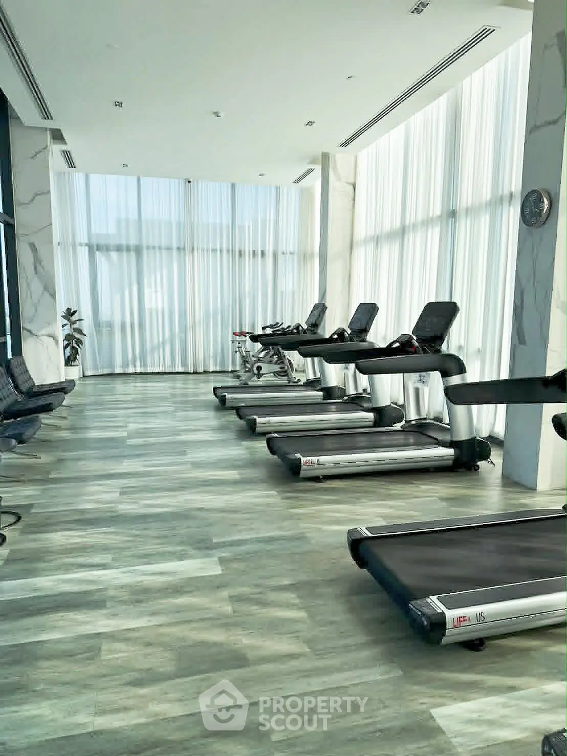 Modern gym with sleek treadmills and floor-to-ceiling windows offering a bright and airy workout space.