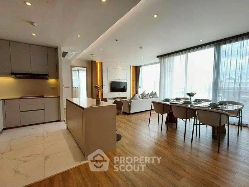 Modern open-plan living room with stylish kitchen and dining area, featuring large windows and elegant decor.