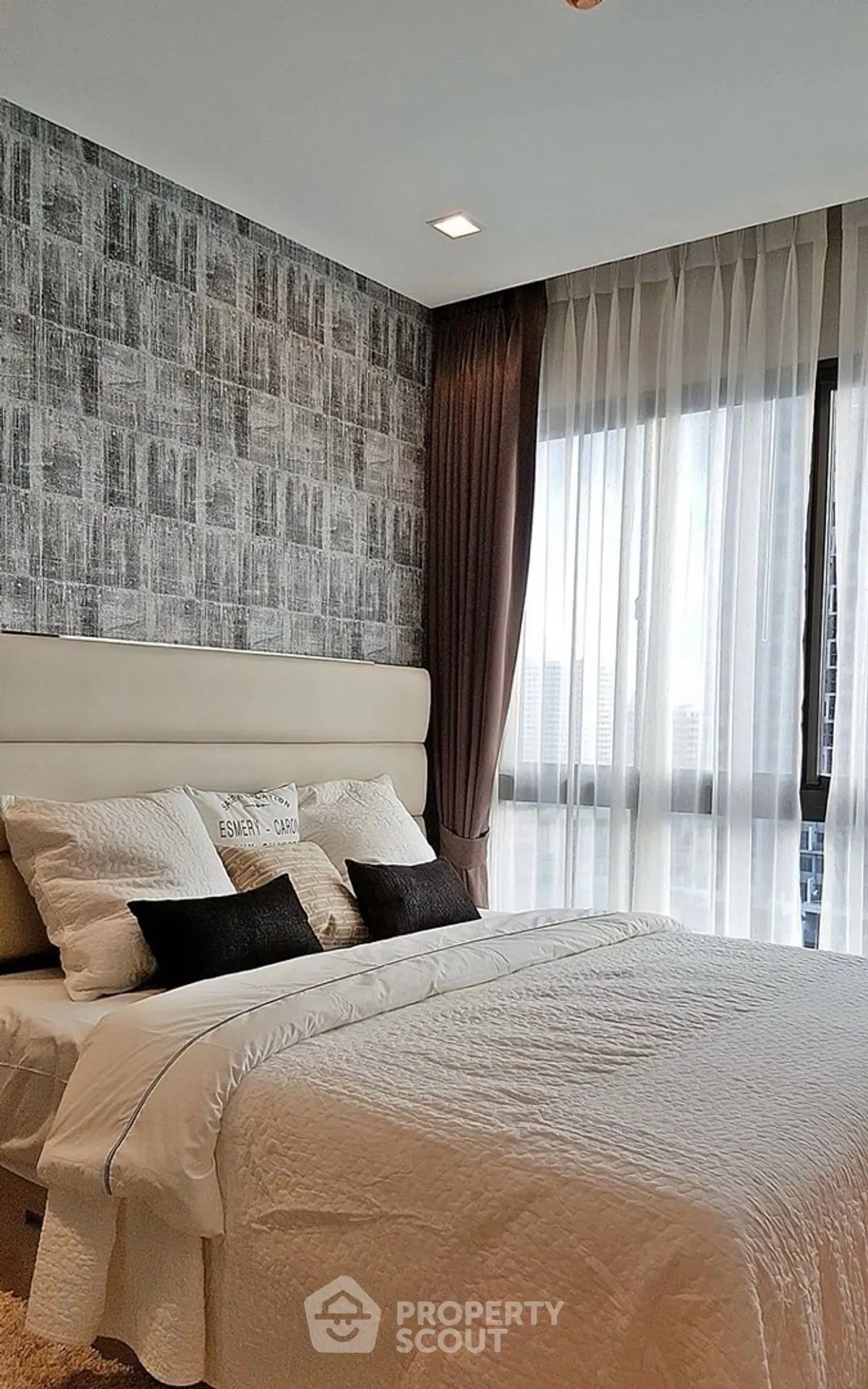 Modern bedroom with stylish decor and large window offering city view.