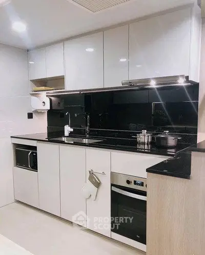 Modern kitchen with sleek cabinetry and built-in appliances, featuring a stylish black backsplash.