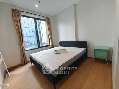 Spacious bedroom with large window and modern furnishings in a high-rise apartment.