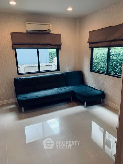 Modern living room with sleek black sofa and large windows offering natural light.