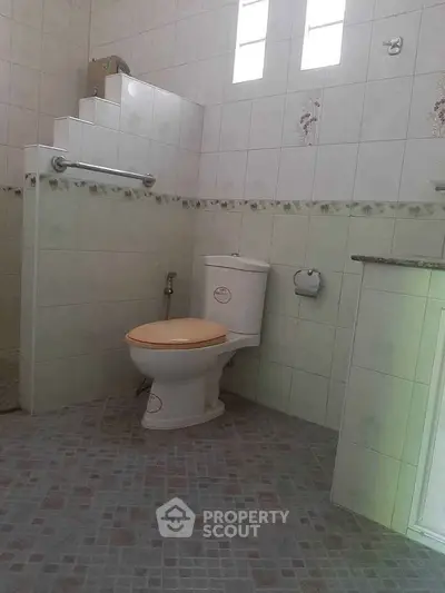 Spacious bathroom with tiled walls and floor, featuring a modern toilet and grab bar.