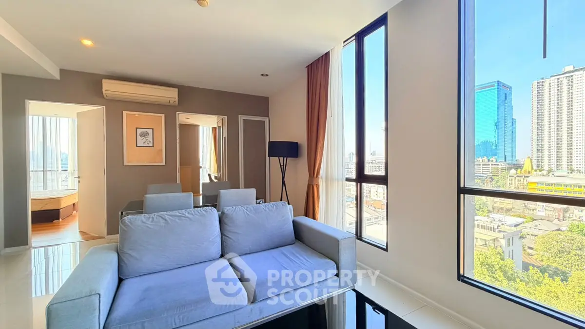 Modern living room with large windows and city view, featuring a cozy sofa and stylish decor.