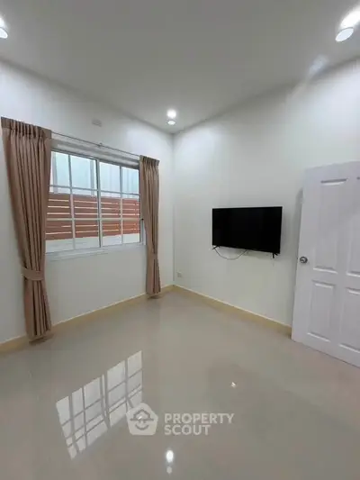 Spacious minimalist room with wall-mounted TV and large window, perfect for modern living.