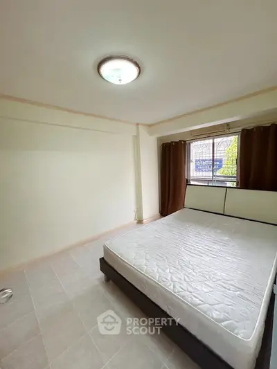 Spacious bedroom with natural light and minimalist design, featuring a large window and neutral tones.