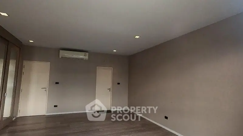 Spacious empty room with wooden flooring and air conditioning, ready for customization.