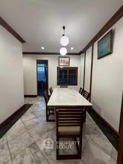 Elegant dining room with marble table and wooden chairs, featuring modern lighting and artwork.