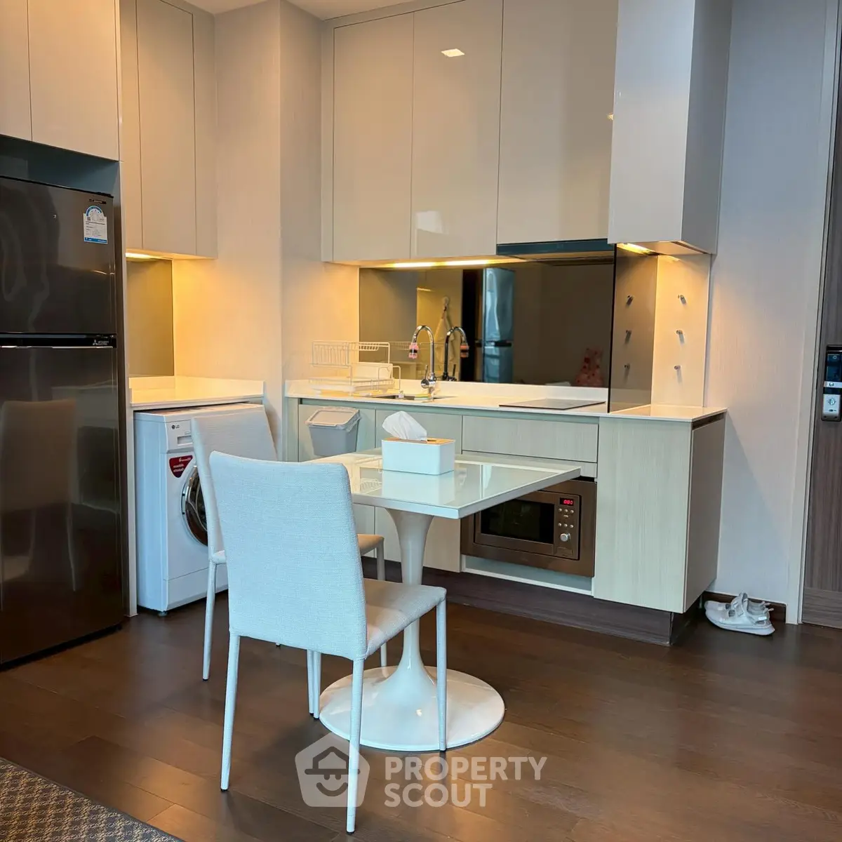 Modern kitchen with sleek cabinets, washing machine, and dining area in contemporary apartment.