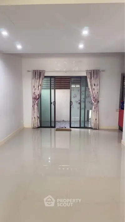 Spacious empty living room with glossy tiled floor and sliding glass doors leading to a balcony.