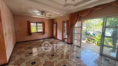 Spacious living room with large windows and garden view, featuring elegant tiled flooring and ceiling fan.