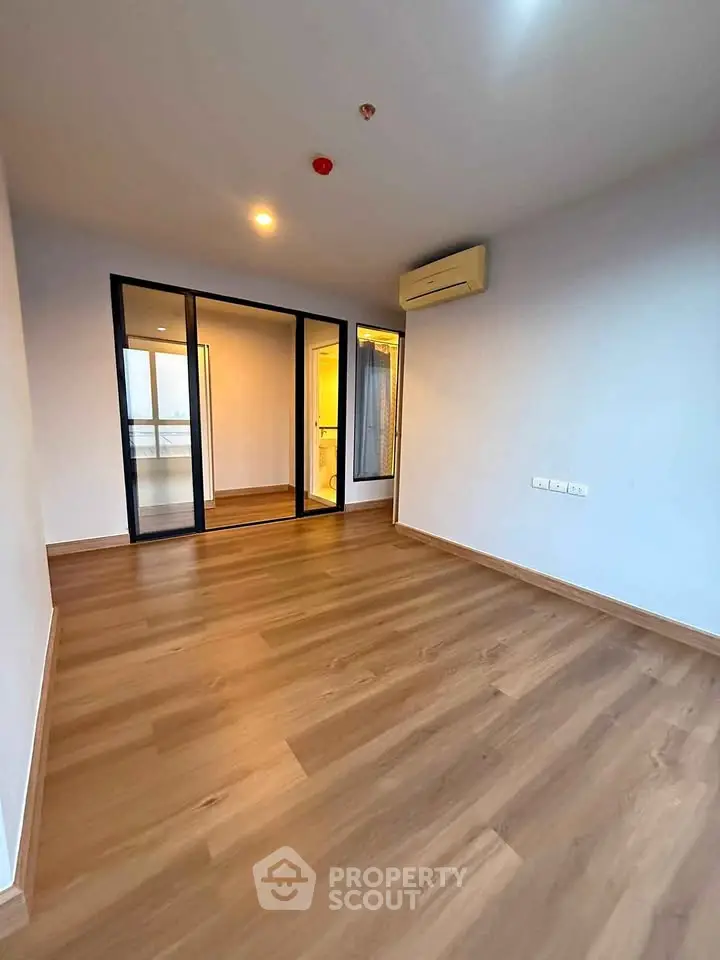 Spacious empty room with wooden flooring and large glass doors, perfect for customization.