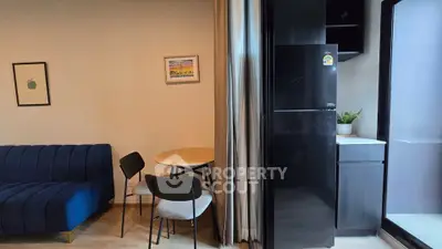 Modern living room with stylish blue sofa, compact dining area, and sleek black refrigerator.