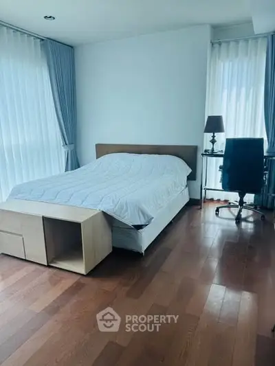 Spacious bedroom with wooden flooring and large windows for natural light