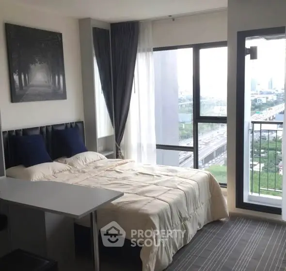 Modern bedroom with large windows offering stunning city view and cozy decor.