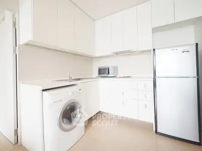 Modern kitchen with sleek white cabinets, washing machine, and fridge in a bright apartment.