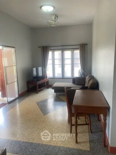 Spacious living room with natural light, featuring a cozy sofa and TV setup, ideal for relaxation.